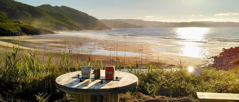 A wooden table with a can of soda and a cup, set on a grassy area with a view of the beach and ocean.