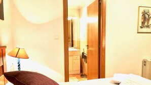 A hotel room with a bed, pillows, a lamp, a bathroom visible through an open door, and a framed picture on the wall. - The Cliffs - Marina Sol te hará soñar (Viveiro)