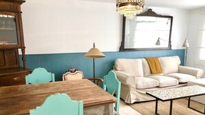 A room with a wooden dining table, teal chairs, a white sofa with a mustard throw, a chandelier, and a large mirror on the wall. - The Cliffs - Le Village Sarridal (Ortigueira)