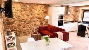 A modern kitchen with stone walls, a dining area with a white table and chairs, and a red sofa. - The Cliffs - Galleon Amieiro (O Vicedo)