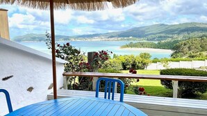 A blue table and chairs under a thatched umbrella on a wooden deck with a view of a coastal landscape. - The Cliffs - A Casa de Mercedes (Mañon)