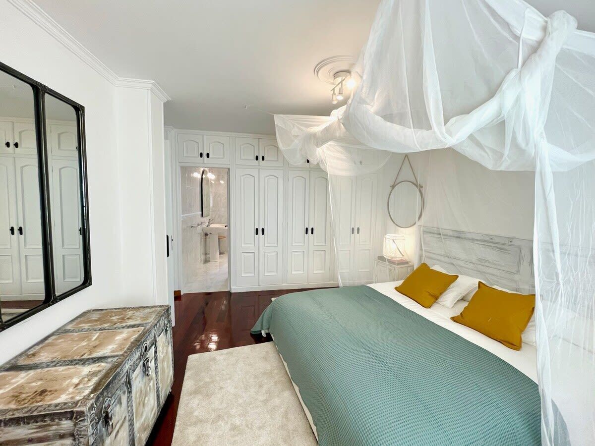 A bedroom with a bed, a nightstand, a dresser, a mirror, and a wardrobe.