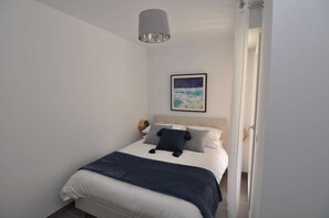 A neatly made bed with a blue blanket and pillows, a hanging light fixture, and a framed picture on the wall.