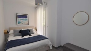 A bedroom with a bed, a bedside table, a lamp, a framed picture, a bench, and a round mirror.