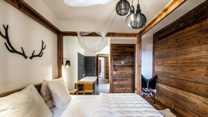 Ein Schlafzimmer mit einem großen Bett, Holzwänden, einer Pendelleuchte und Blick in ein weiteres Zimmer mit einer Badewanne.