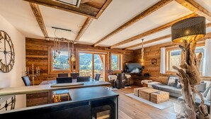 Ein rustikales Blockhaus-Interieur mit Holzwänden, einem Essbereich, einem Wohnzimmer mit Sofa und einem großen Fenster mit Blick auf die Berge.
