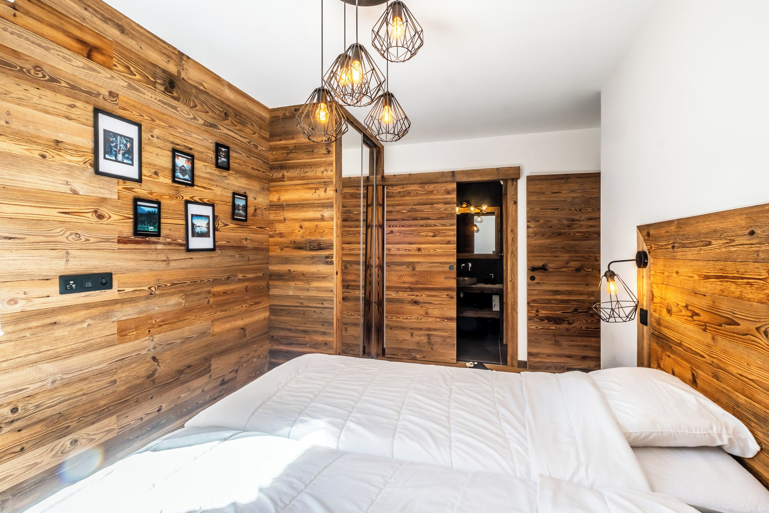 Un dormitorio con paredes de madera, una cama con ropa de cama blanca y una lámpara colgante.