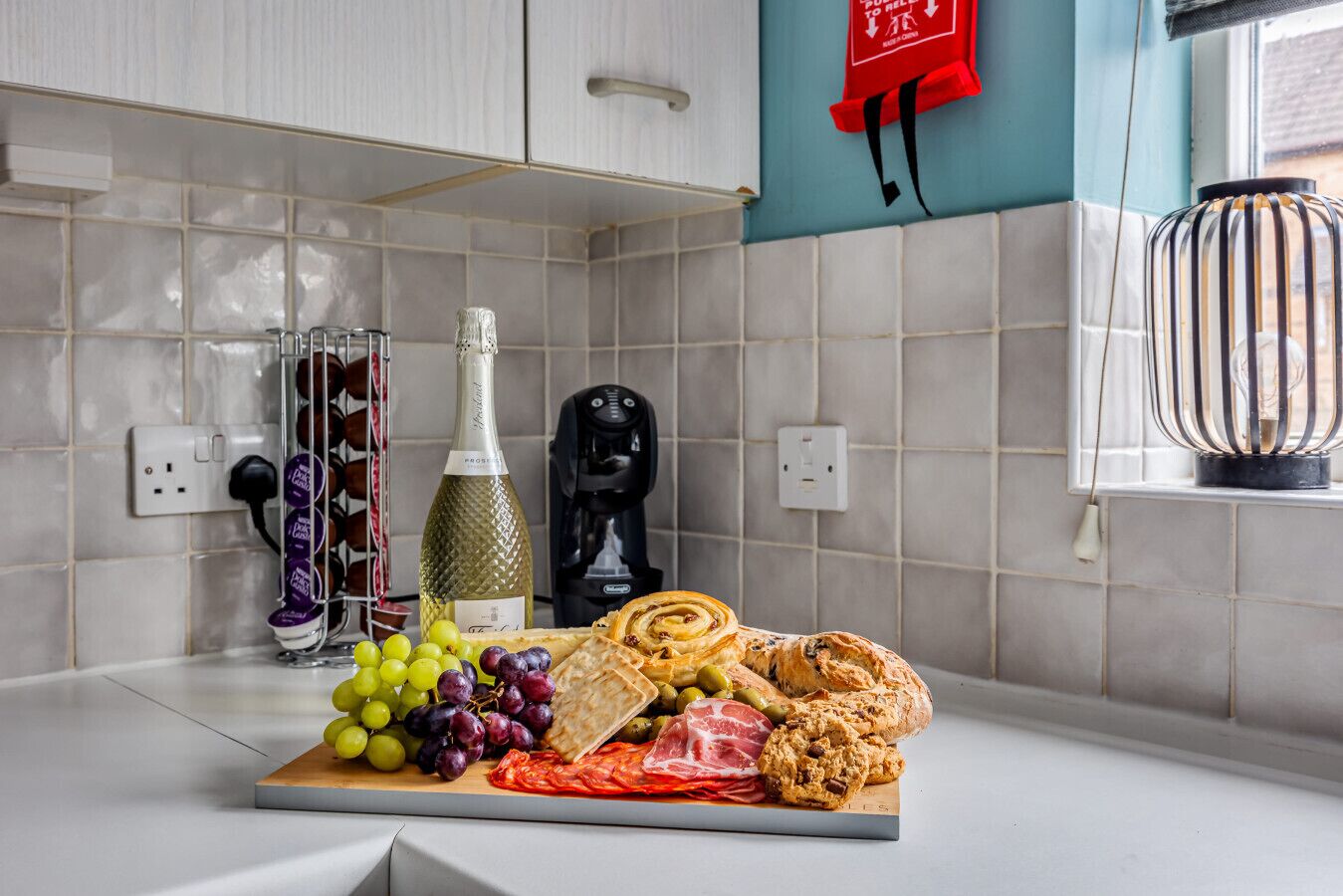 A kitchen counter with a variety of food items including grapes, olives, a bottle of wine, a loaf of bread, and a chocolate cookie.
