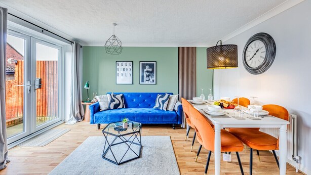 A modern living room with a blue sofa, dining table, and chairs, a glass coffee table, and a large window.