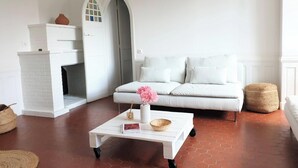 A living room with a white sofa, a white coffee table, a fireplace, and a tiled floor. - Charming Renovated Cottage in 2-Hectare Park with Fishing Pond, Near Forest, Close to Versailles (Senlisse)