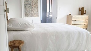 A bedroom with a large bed, a wooden stool, a dresser, and a cactus decoration. - Charming Renovated Cottage in 2-Hectare Park with Fishing Pond, Near Forest, Close to Versailles (Senlisse)