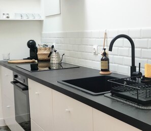 A modern kitchen with a black countertop, white cabinets, a black sink, and a coffee machine. - Charming Renovated Cottage in 2-Hectare Park with Fishing Pond, Near Forest, Close to Versailles (Senlisse)
