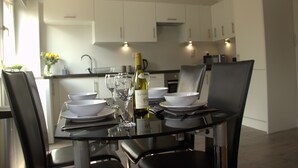 Una zona de menjador moderna amb una taula de vidre preparada per a quatre, plats blancs, bols i copes de vi.