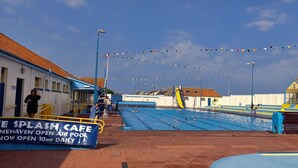Una piscina descoberta amb un solàrium blau i groc, envoltada d'edificis i un cel serè.