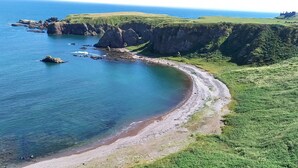 Paisatge costaner amb penya-segats, una platja i una zona verda.