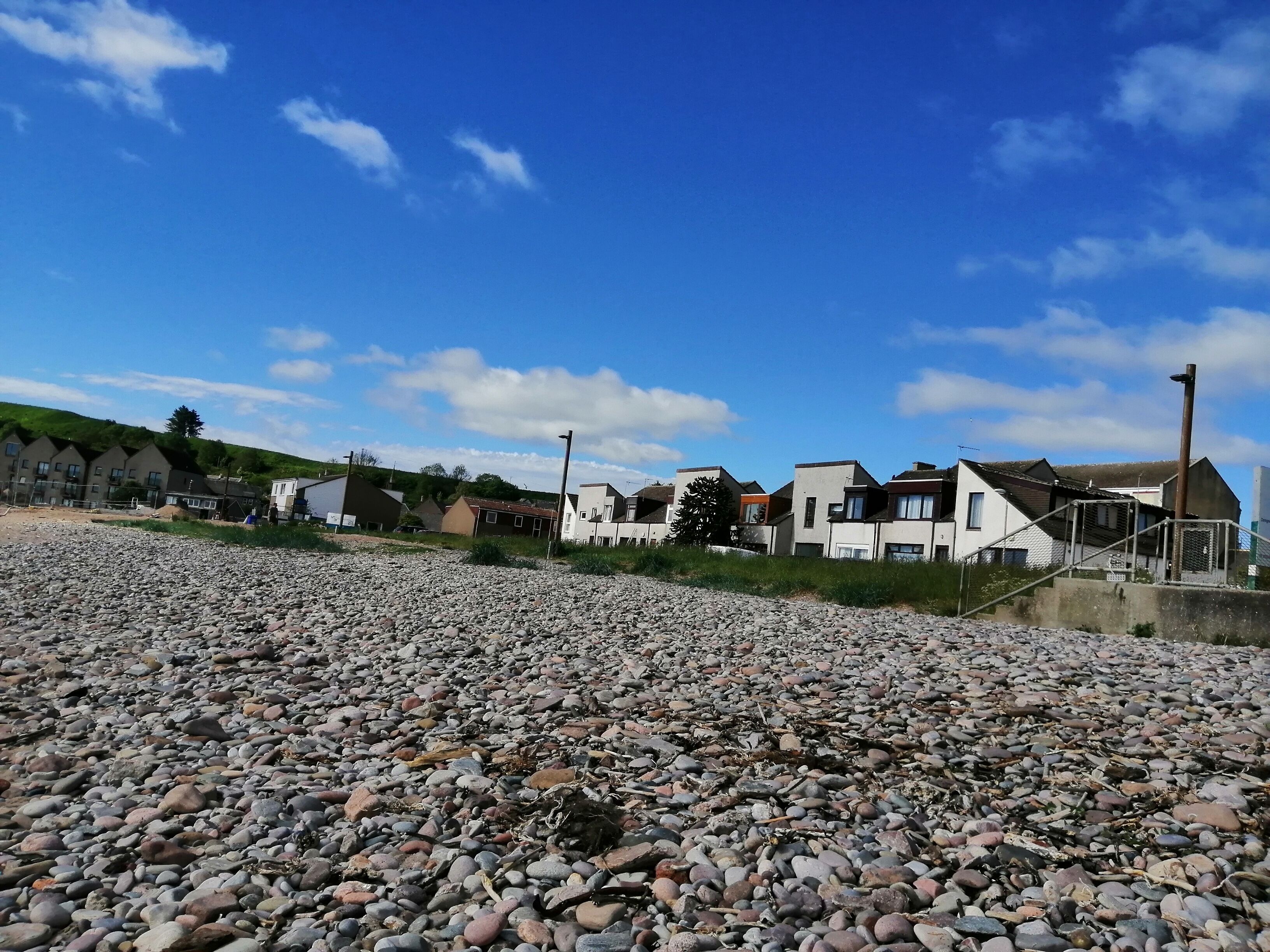 A pebbled beach with modern houses in the background.