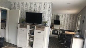 Una cocina moderna con horno y microondas integrados, un comedor con mesa de madera y un espacio de sala de estar con televisor montado en un mueble.