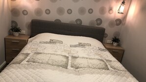 Un dormitorio con cama, dos mesitas de noche, una lámpara de pared y papel tapiz estampado.