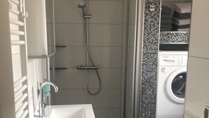 Un baño pequeño con un lavabo blanco, ducha y lavadora.