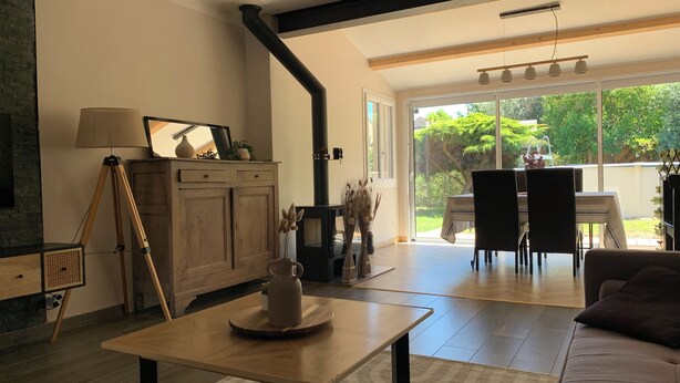 A living room with a wooden table, sofa, and a fireplace. There is a dining area with a table and chairs visible through a glass door. - Cosy house in peaceful setting 10 minutes from Avignon (Le Pontet)