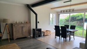 A modern living room with a wooden cabinet, a black stove, a dining table with chairs, and a large window with a view of greenery. - Cosy house in peaceful setting 10 minutes from Avignon (Le Pontet)