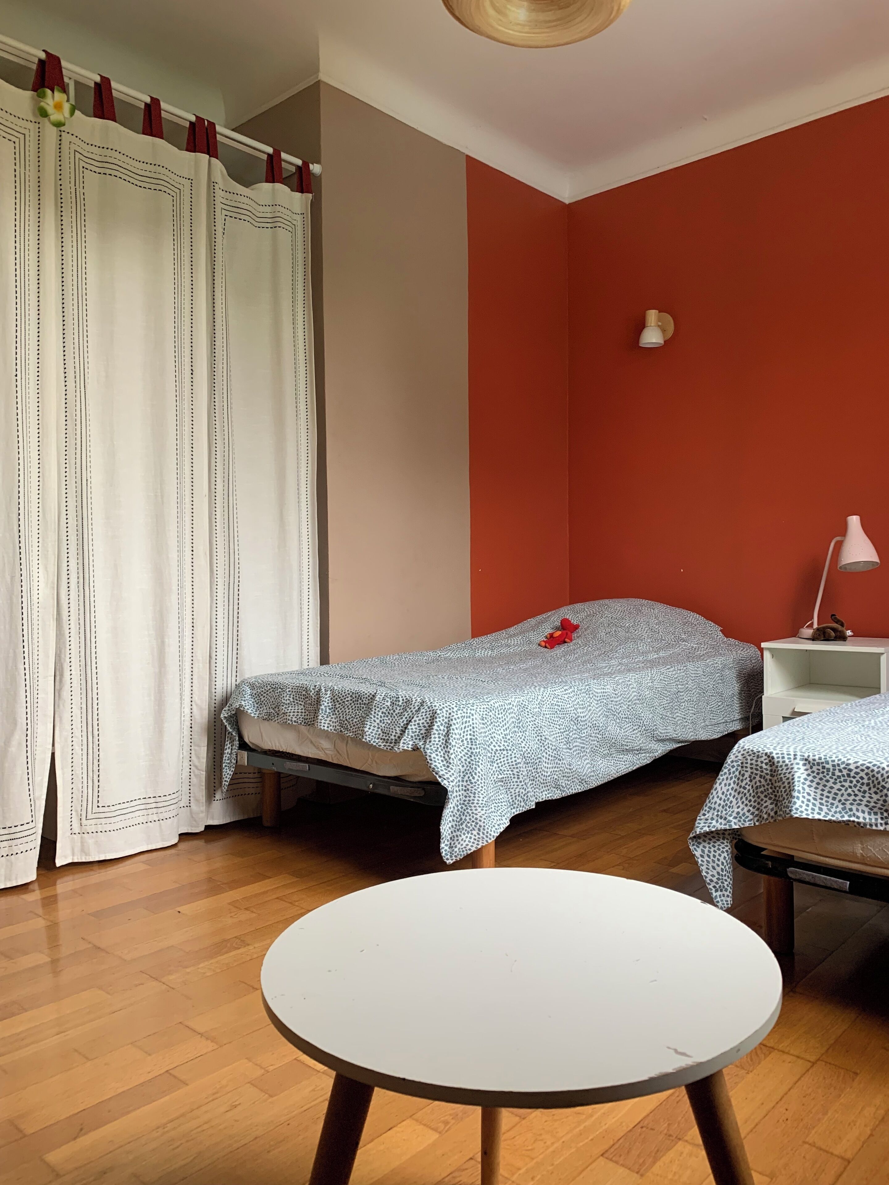 Een kleine kamer met een bed, een tafel en een rode wand.