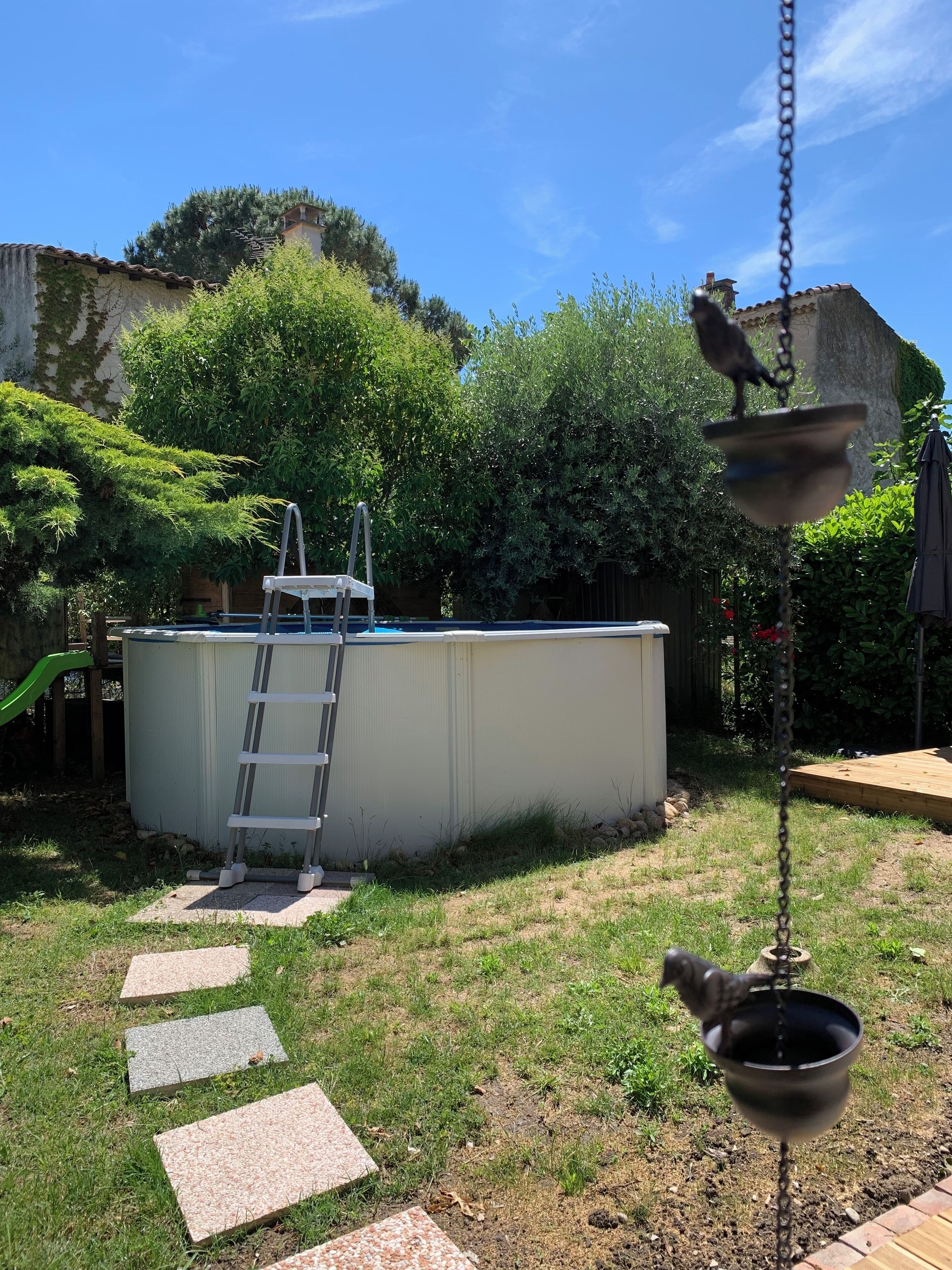 Un patio trasero con piscina, una escalera, piedras y una maceta colgante.
