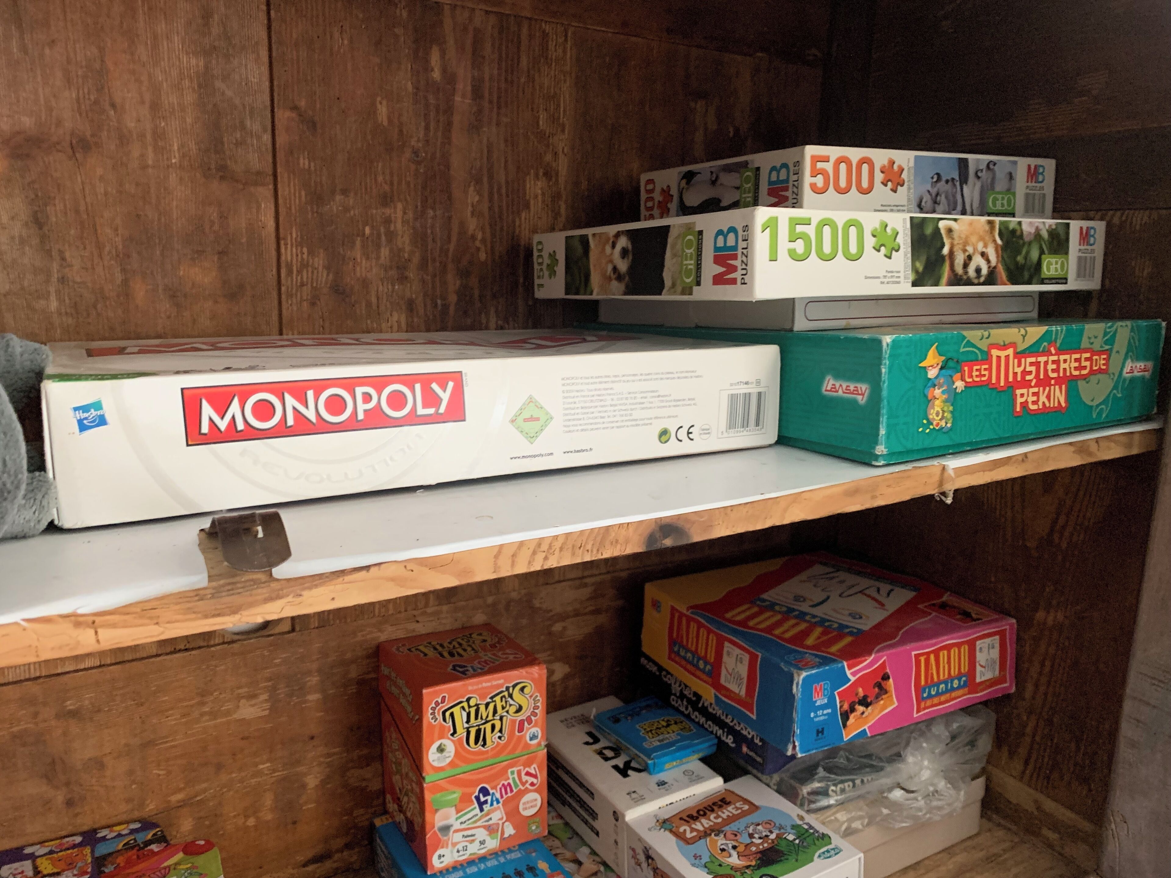 A shelf with various board games including Monopoly, Les Mystères de Pekin, and Taboo Junior.