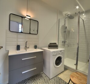A modern bathroom with a dual sink vanity, a washing machine, a glass shower enclosure, and a patterned floor. - Magnificent T2 hyper center, hyper equipped (La Rochelle)