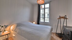 A bedroom with a bed, bedside table, lamp, window, and a drying rack. - Magnificent T2 hyper center, hyper equipped (La Rochelle)