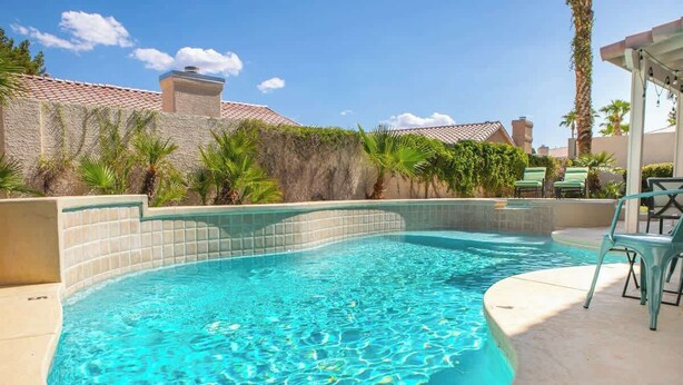 A swimming pool with a tiled edge, surrounded by palm trees and a stone wall. - ❤️New 4BR/3Ba with Pool, 9 miles to LV Strip! (Henderson)