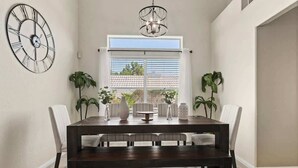 A dining room with a dark wooden table, white chairs, a large wall clock, and a chandelier. - ❤️New 4BR/3Ba with Pool, 9 miles to LV Strip! (Henderson)