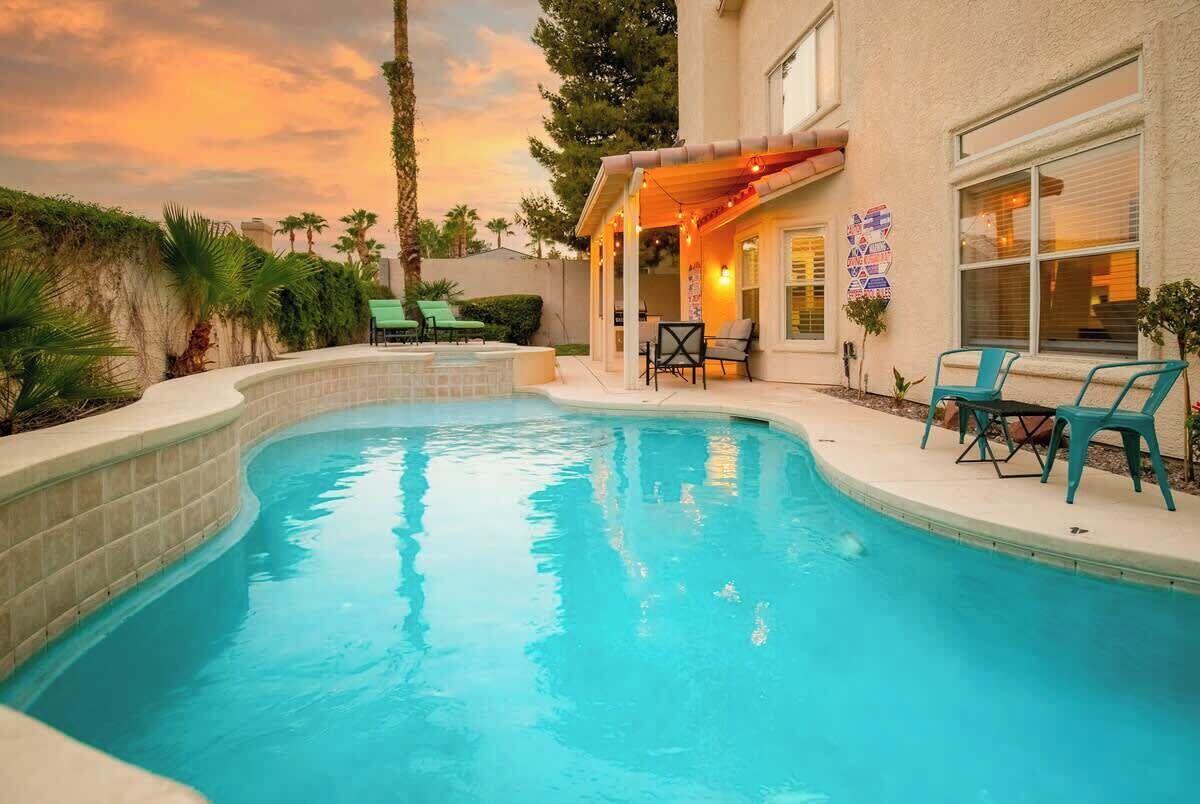 Ein Pool mit geschwungener Kante, umgeben von einer Terrassenfläche mit Stühlen und einer überdachten Sitzgelegenheit.