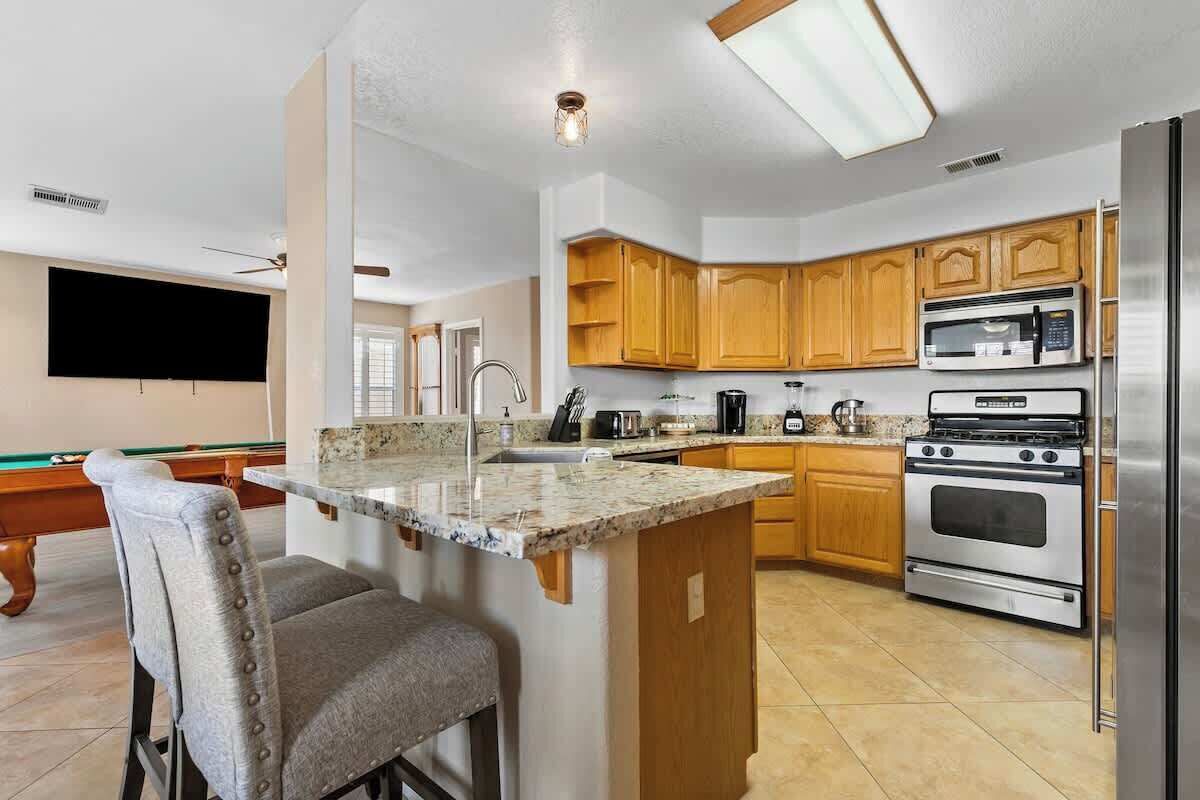 A kitchen with wooden cabinets, a stainless steel refrigerator, a microwave, and an oven. There is a bar area with stools.