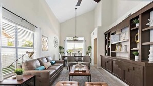 A spacious living room with a brown leather sofa, a wooden coffee table, and a dining area with a chandelier. - ❤️New 4BR/3Ba with Pool, 9 miles to LV Strip! (Henderson)