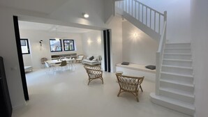 Amplia sala de estar con una escalera blanca, una mesa de comedor con sillas y un sofá.
