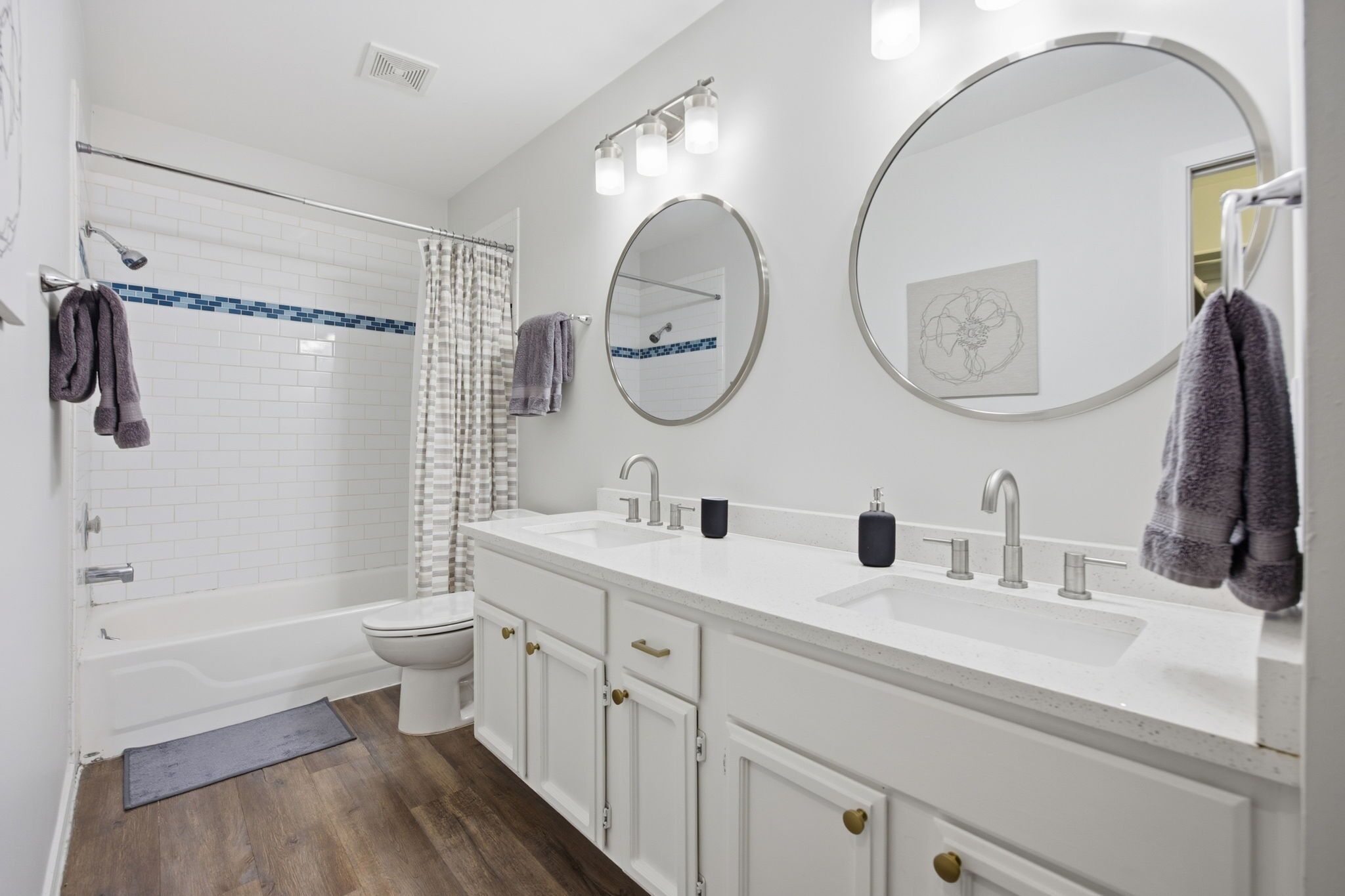 A modern bathroom with a white vanity, two sinks, a toilet, and a shower area.