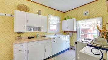 A kitchen with white cabinets, a sink, and a stove. There is a window with a floral curtain and a basket on the wall.