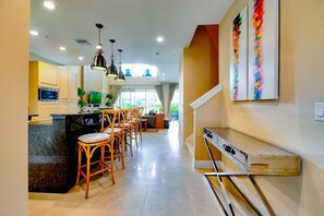 A modern kitchen with a central island, wooden chairs, and pendant lighting.