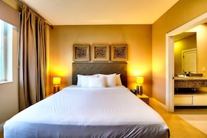 A hotel room with a large bed, two bedside lamps, a headboard with three framed pictures, and a bathroom visible through an open door.
