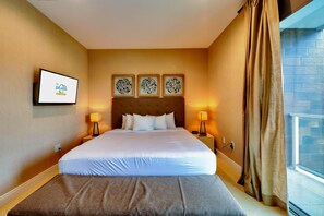 A hotel room with a large bed, two bedside lamps, a flat-screen TV, and three wall art pieces above the bed.