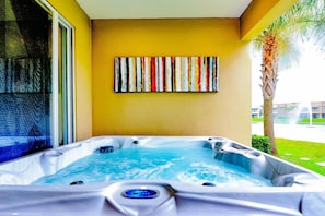 A hot tub with a control panel, a colorful abstract painting on the wall, and a palm tree outside.