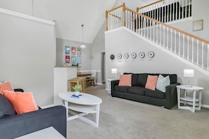A modern living room with a staircase, a dining area, and a wall with clocks. - Calypso Villa (Kissimmee)