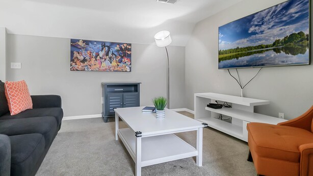 A modern living room with a flat-screen TV, a painting, a fireplace, and a coffee table. - Calypso Villa (Kissimmee)