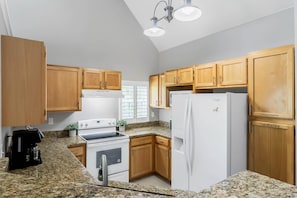 A kitchen with wooden cabinets, a white refrigerator, a stove, and a coffee maker. - Calypso Villa (Kissimmee)
