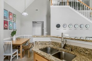 A modern kitchen with granite countertops, a stainless steel sink, and a dining area with a wooden table and chairs. - Calypso Villa (Kissimmee)