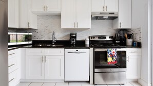 A modern kitchen with white cabinets, a dishwasher, an oven, and a coffee maker. - Pearl Villa (Kissimmee)