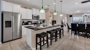A modern kitchen with white cabinets, stainless steel appliances, and a central island with bar stools. - Luxurious Vacation Home With Private Pool!!! (Kissimmee)