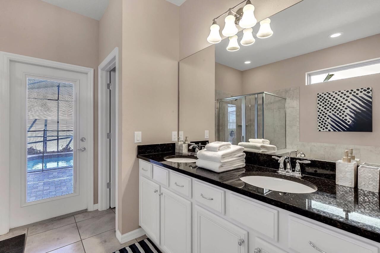 A modern bathroom with a large mirror, a glass shower enclosure, and a black countertop.