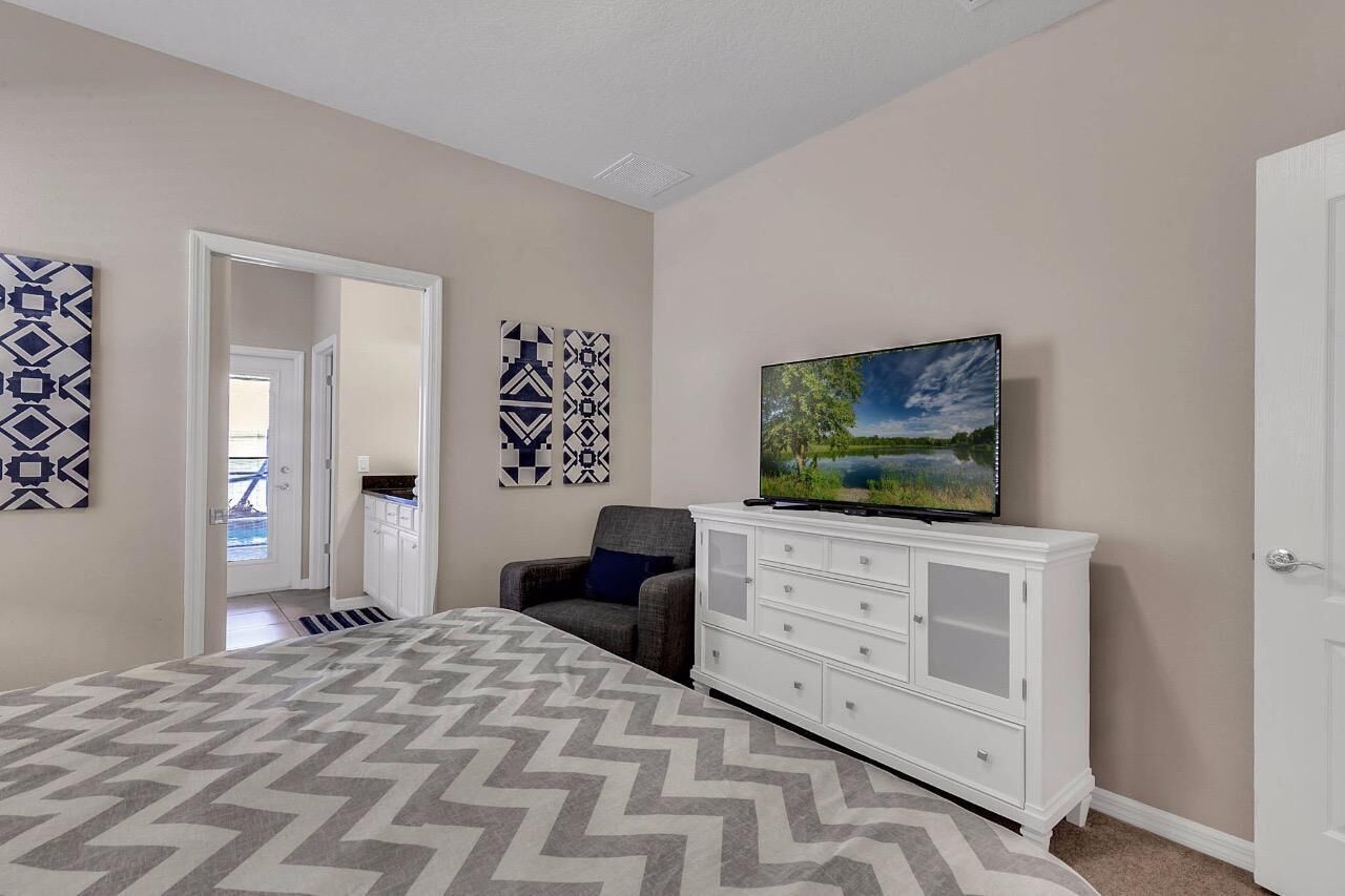 A bedroom with a bed, a TV, a white dresser, and patterned wall art.